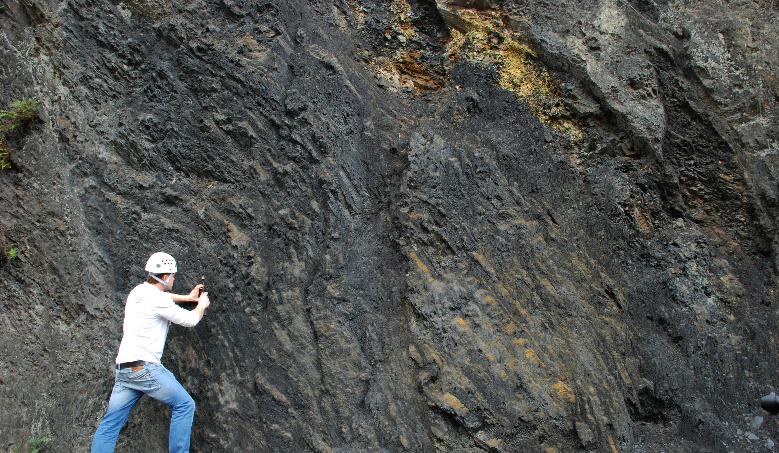 Geologist wearing a hard hat, examining a rock outcrop with a geological hammer.